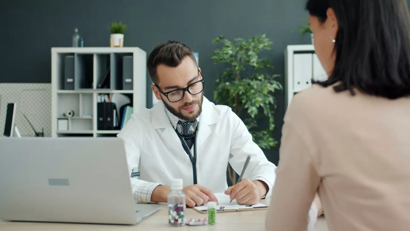 Le médecin prend des notes tandis que le patient est assis en face.
